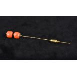 An unmarked gold coral bead mounted stick pin Set with two coral beads. 10.25 cm long.