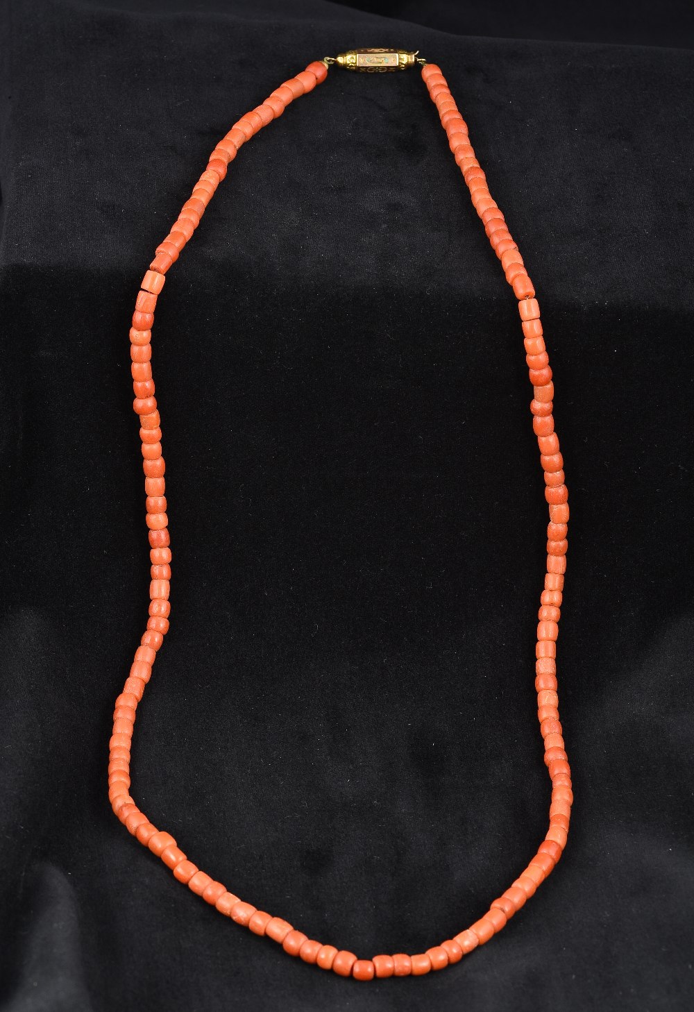 A single strand coral bead necklace Set with an enamel decorated unmarked yellow metal clasp.