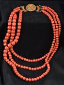 A large three strand coral bead necklace Set with a cabochon mounted pierced gold clasp.