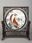 A Chinese porcelain inset carved wooden table screen The revolving central panel painted with a