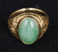 An 18K gold and jade ring Centrally set with a jade cabochon above the engraved shoulders. 1.