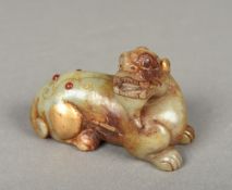 A Chinese carved and russet jade gilt decorated and gem set temple lion Modelled recumbent.