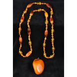 A large polished butterscotch amber pendant Together with an amber bead necklace. The former 6.