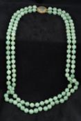 A Chinese two strand jade bead necklace Set with a carved jade centred pierced 14K gold clasp.