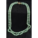 A Chinese two strand jade bead necklace Set with a carved jade centred pierced 14K gold clasp.