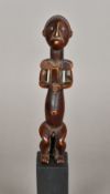 An African tribal carved wooden figure Formed as a seated male, mounted on a later display plinth.