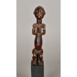 An African tribal carved wooden figure Formed as a seated male, mounted on a later display plinth.