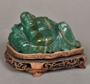 A Chinese carved green stone Buddha Modelled recumbent, on a carved wood plinth base.