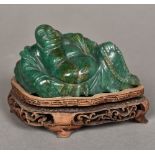 A Chinese carved green stone Buddha Modelled recumbent, on a carved wood plinth base.