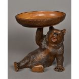 A Black Forest carved bear Modelled recumbent, holding aloft a bowl inscribed Interlaken.