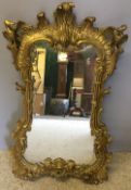 A 19th century carved giltwood wall glass The floral and scroll carved frame topped with scroll