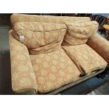 A pink upholstered two seater sofa with lozenge decoration resting on squat supports