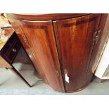 A Georgian mahogany and oak bow front corner cabinet the double doors enclosing three shelves