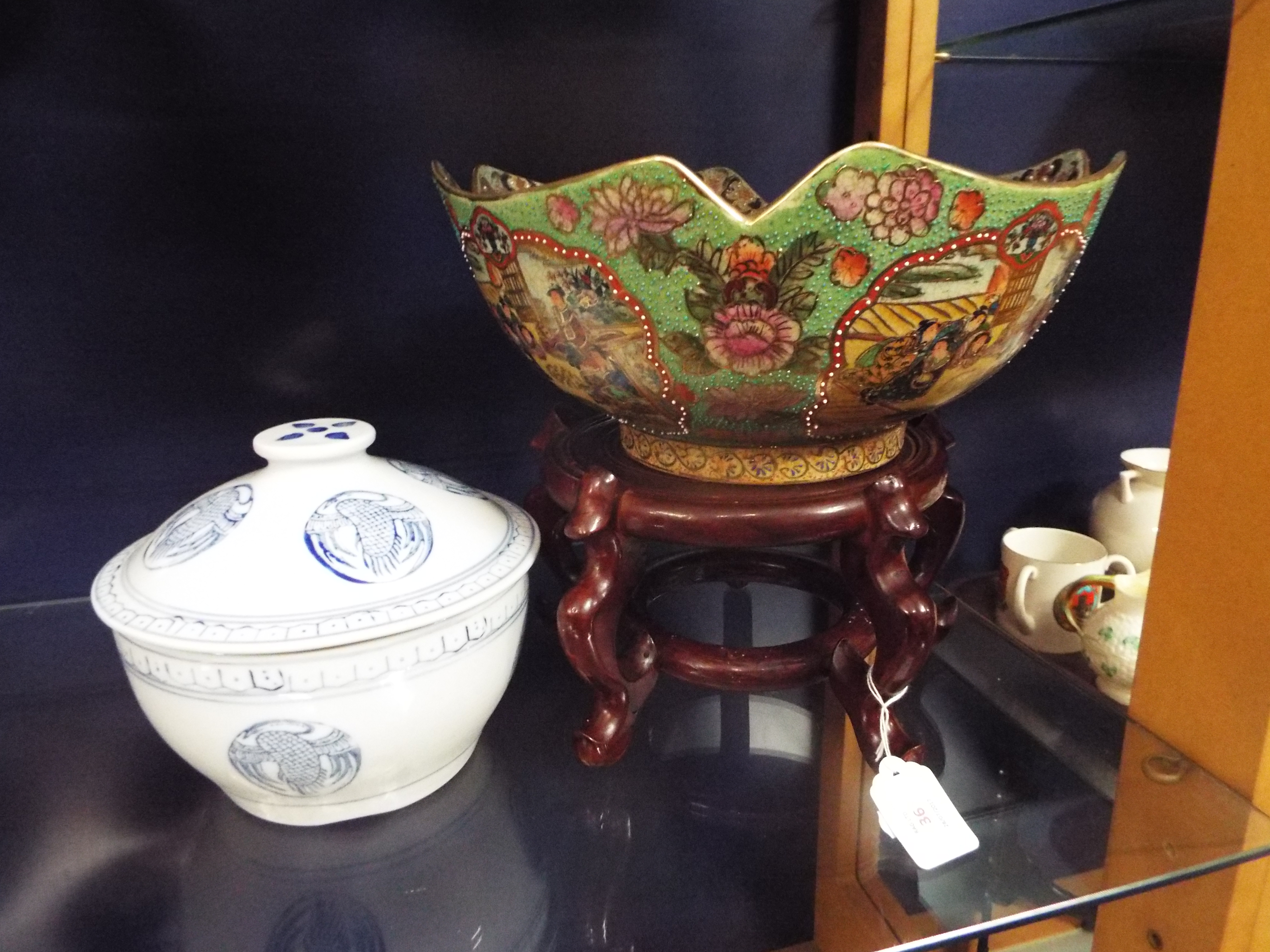 A large Satsuma style famille verte bowl decorated with geisha and bonsai resting on a hardwood