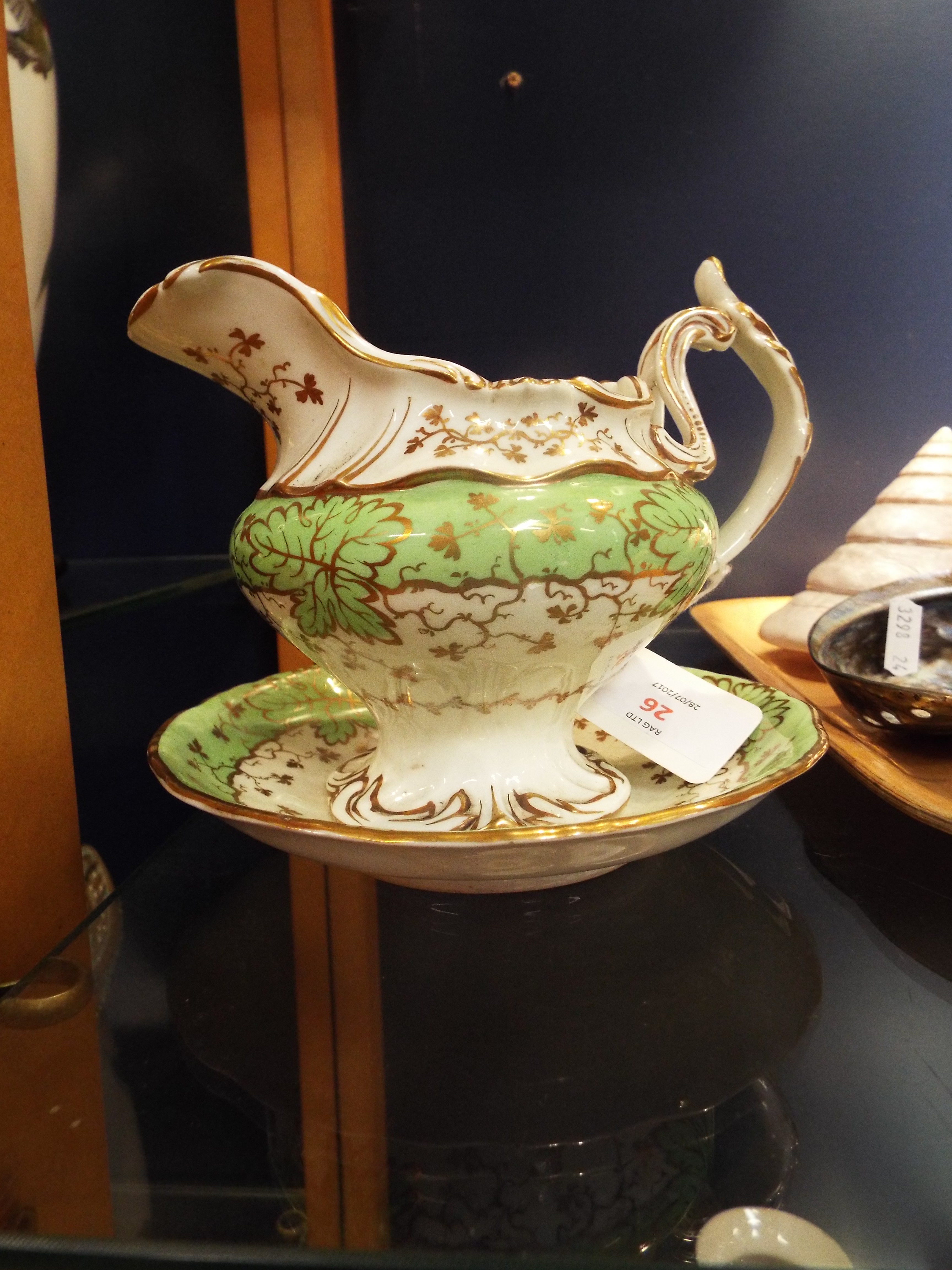 A Rockingham style cream jug and stand decorated with gilt vines and leaves with green and white