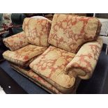 A beige ground floral upholstered two seater sofa raised on bun feet