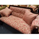 A carved oak framed three seater with red floral upholstery