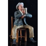 An Austrian Bernard Bloch painted pottery figure of a seated man holding a mug of beer, seated on