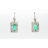 A pair of unmarked white gold emerald & diamond earrings, each with a rectangular cut emerald within