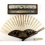 A late 19th / early 20th century gilt decorated black lacquer & embroidered silk fan, in fitted