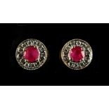 A pair of yellow gold ruby & diamond stud earrings, each with a round cut ruby set within a border