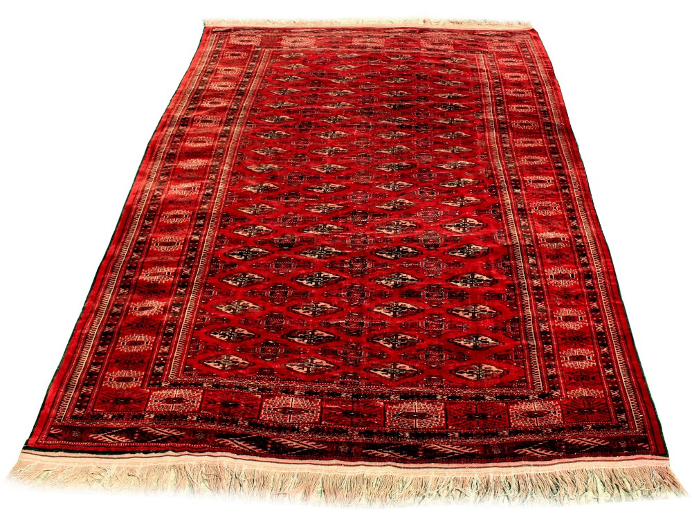 A Turkoman woollen hand-made rug with red ground, 114 by 78ins. (289 by 197cms.) (see