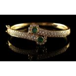 An unmarked yellow gold emerald & diamond hinged crossover bracelet, set with two round cut