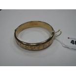 A 9ct Gold Bangle, leaf scroll engraved to the front, hinged to snap clasp.