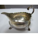 A Hallmarked Silver Sauce Boat, with wavy rim and flying scroll handle, raised on three shell capped