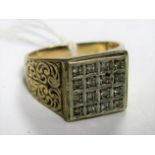 A 9ct Gold Gent's Ring, the square panel sixteen stone inset, between scroll textured shoulders.