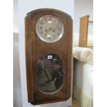 A 1920's Oak Wall Clock, with a silvered dial, oval bevelled glass panel, chrome pendulum, stepped