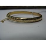 A 9ct Gold Bangle, leaf scroll engraved to the front, hinged to snap clasp.