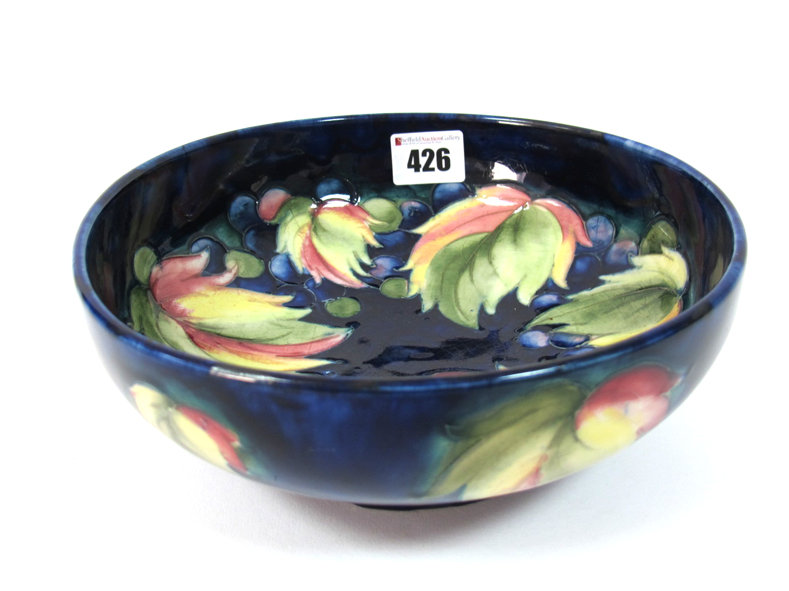 A 1930's Moorcroft Pottery Footed Bowl, painted in the Leaf and Berry pattern against a dark blue