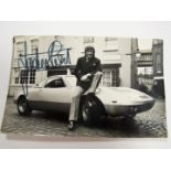 Jackie Stewart Autograph, black pen signed on a 1970's photo of him, sat on the bonnet of a sports