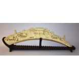 A faux ivory tusk, intricately carved with pagodas in landscape, on hardwood stand,