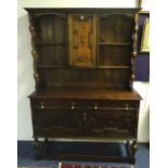 A Jacobean style oak dresser, the top section with panelled door flanked by open shelves,