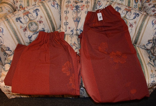A pair of red fabric curtains, decorated with floral panels,