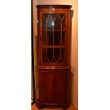 A reproduction corner cabinet, with glazed door enclosing shelved interior above panelled door,