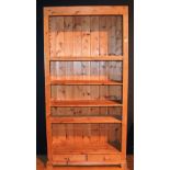 A tall pine open bookcase, with open shelving above two small drawers,