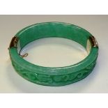 A Chinese green jade and 14ct gold mounted bangle, the mint green jade with carved foliate relief,