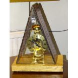 A modern skeleton mantel clock, within triangular glass cover, raised on oak plinth base,