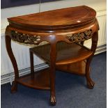 A Chinese hardwood demi-lune occasional table, with carved foliate frieze above open shelving,