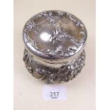 A large circular silver toiletry box with all over embossed decoration and cupid to lid, by the