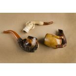 Two carved meerschaum pipe bowls, both bowls carved with claws and eggs, one with curved amber
