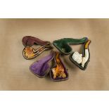 Three cased meerschaum cheroot holders, each bowl with carved mask and amber mouth pieces, one