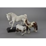 A small group of Beswick horses, including Spirit of Freedom, a skewbald pony, and a matt grey