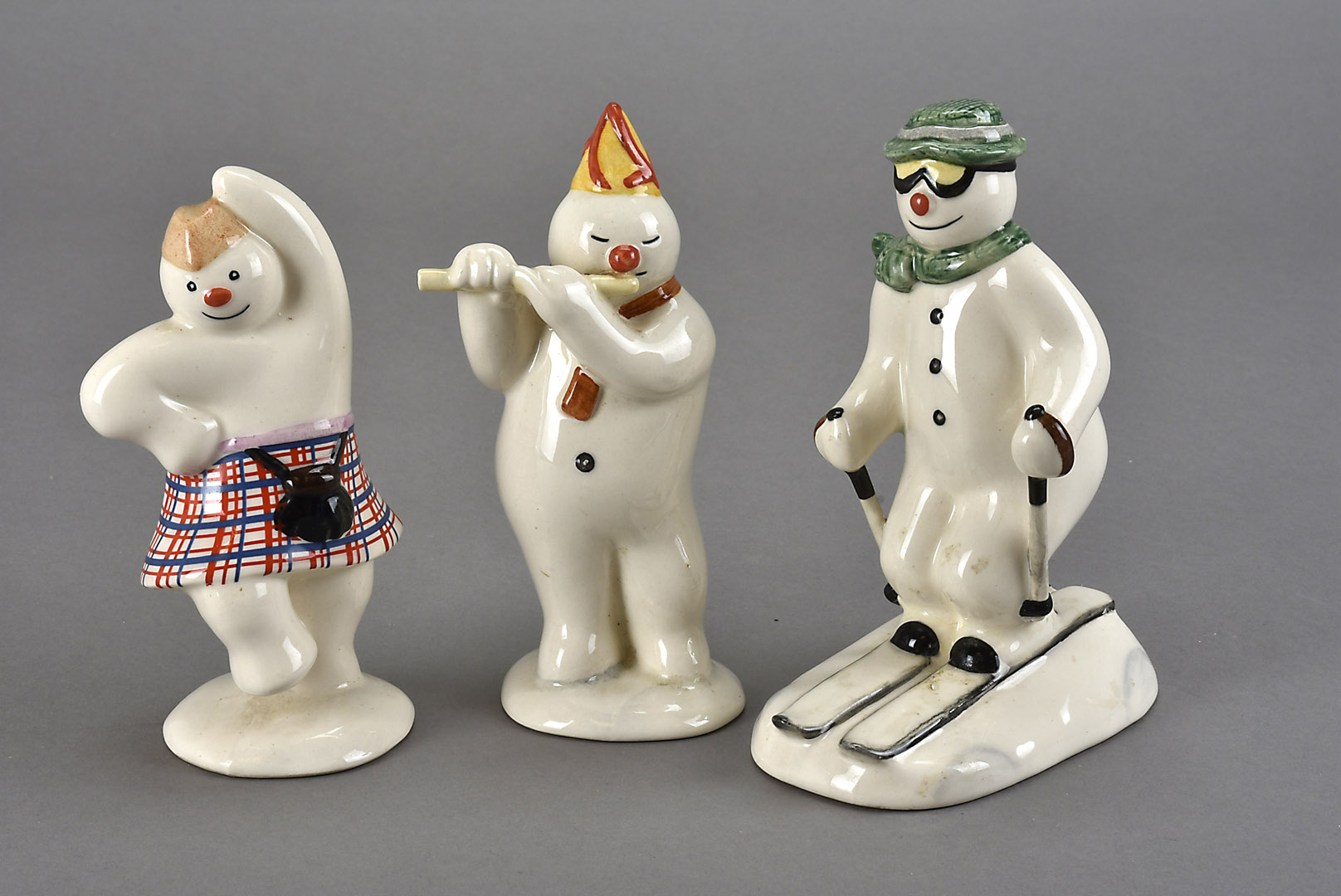 Three Royal Doulton 'Snowman' figures, one as a downhill skier AF, a flautist, and a jigging