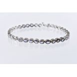 A modern 9ct white gold and tanzanite line bracelet, the light blue oval stones in tennis style