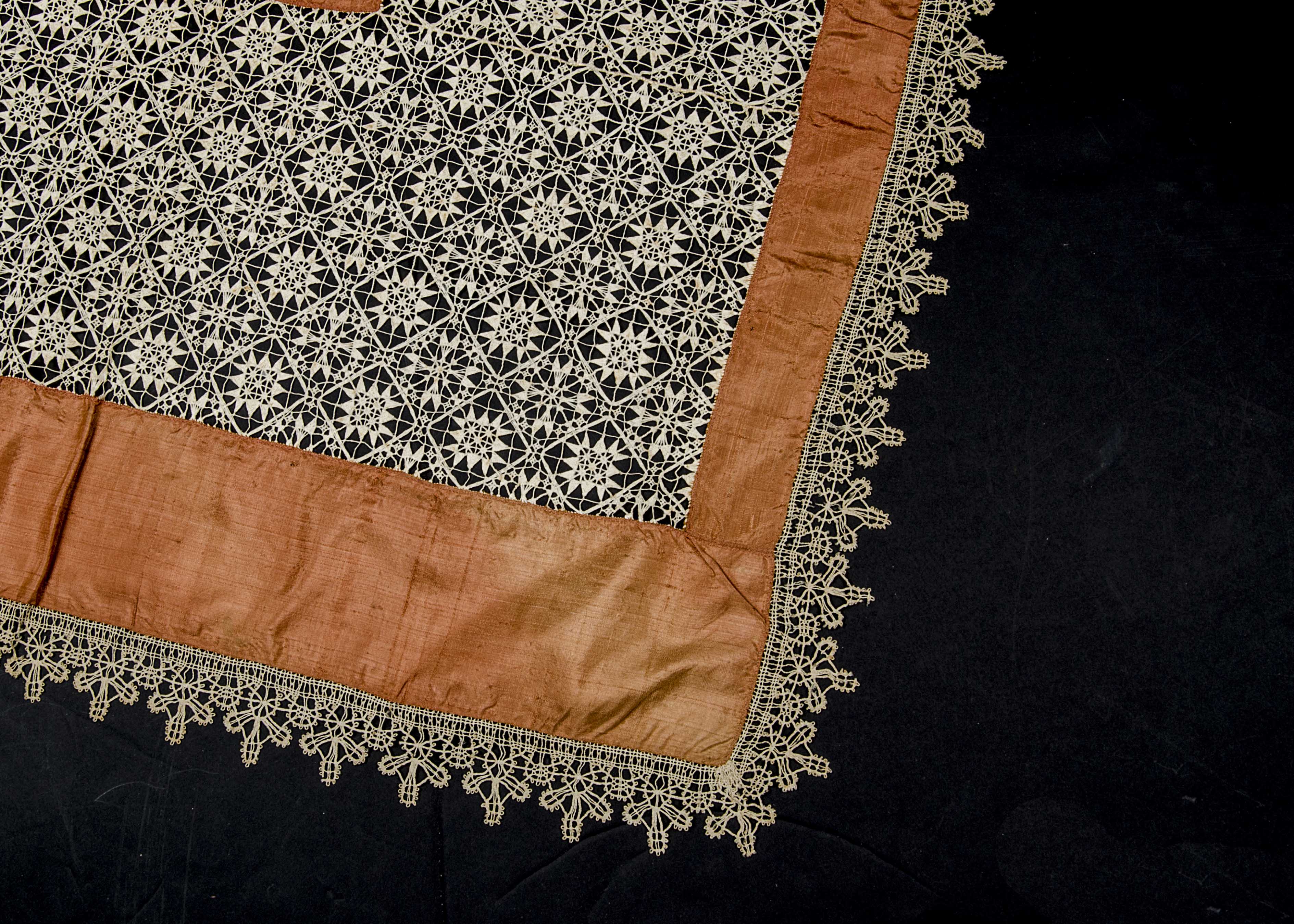 An 1880s table cover of brown silk, inset with reticella-type cotton lace, the border of bobbin lace