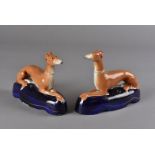 A pair of Staffordshire pen holders, modelled as recumbent greyhounds on deep blue cushions 16.5